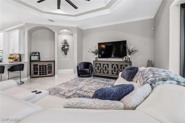 living room with ceiling fan, a tray ceiling, and ornamental molding