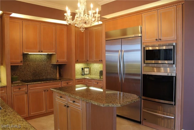 kitchen with tasteful backsplash, a center island, hanging light fixtures, light stone countertops, and built in appliances