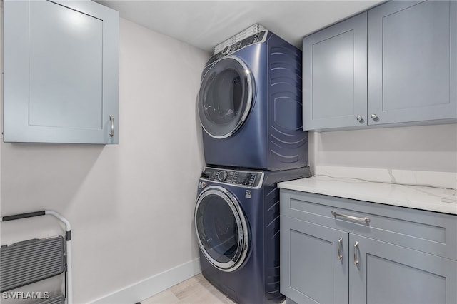 laundry room featuring stacked washer / dryer, cabinet space, and baseboards