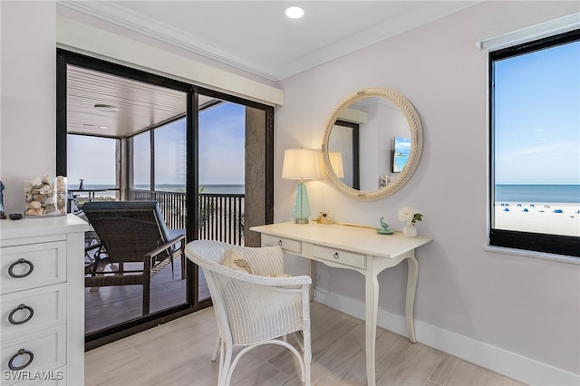 home office with baseboards, a water view, crown molding, light wood-style floors, and a view of the beach