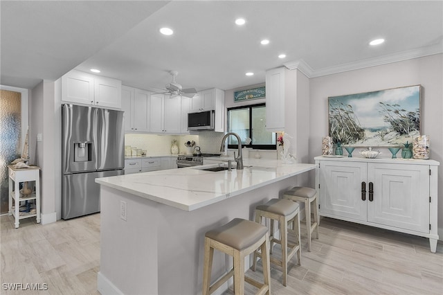 kitchen with a peninsula, appliances with stainless steel finishes, white cabinets, and a sink