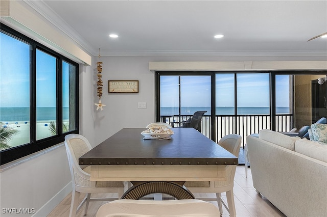 dining area featuring crown molding, a water view, light wood-style flooring, and a healthy amount of sunlight