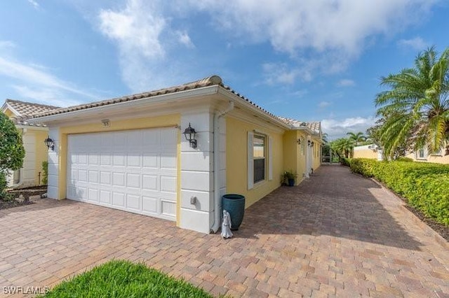 view of property exterior with an attached garage, decorative driveway, and stucco siding