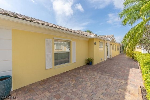 view of property exterior featuring a garage, a tiled roof, a patio, and stucco siding