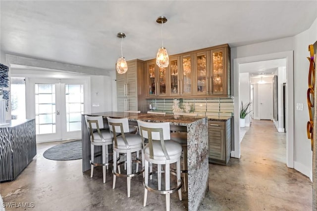 kitchen featuring concrete floors, french doors, brown cabinets, dark stone countertops, and decorative light fixtures