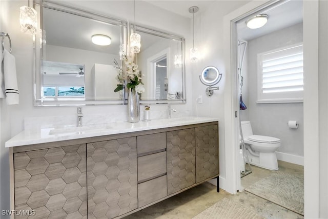 bathroom featuring double vanity, toilet, ceiling fan, a sink, and baseboards