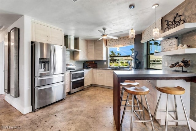 kitchen with dark countertops, stainless steel appliances, wall chimney range hood, a kitchen bar, and open shelves