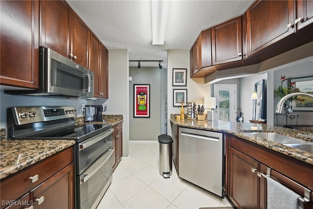 kitchen featuring stainless steel appliances, a textured ceiling, dark stone counters, light tile patterned floors, and sink