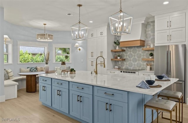 kitchen with white cabinets, stainless steel fridge, pendant lighting, and premium range hood