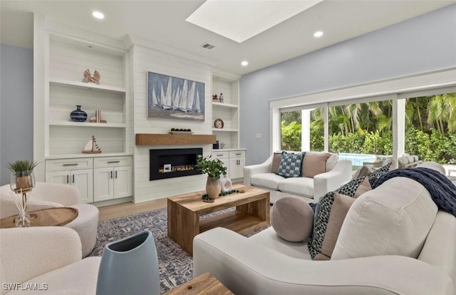 living room with a warm lit fireplace, a skylight, built in features, wood finished floors, and recessed lighting