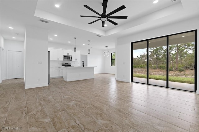 unfurnished living room featuring a tray ceiling, sink, and ceiling fan