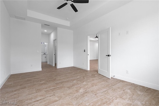 unfurnished bedroom with a raised ceiling, ceiling fan, and ensuite bath