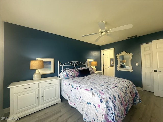 bedroom with a ceiling fan, visible vents, baseboards, and wood finished floors