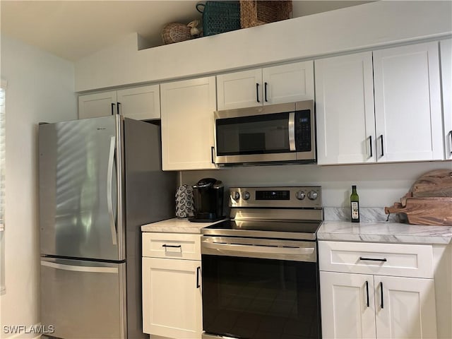 kitchen with appliances with stainless steel finishes, lofted ceiling, white cabinets, and light stone countertops