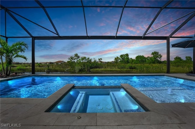 pool at dusk featuring a patio area, a pool with connected hot tub, and glass enclosure