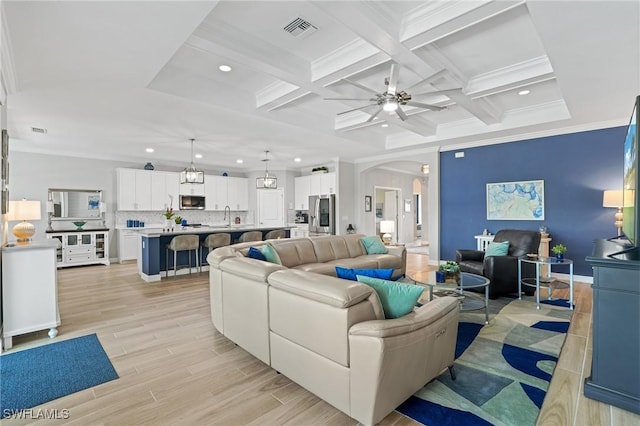 living room featuring arched walkways, visible vents, light wood-type flooring, beam ceiling, and crown molding