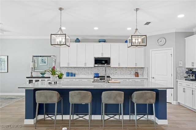 kitchen featuring an island with sink, stainless steel microwave, visible vents, and light wood-style floors