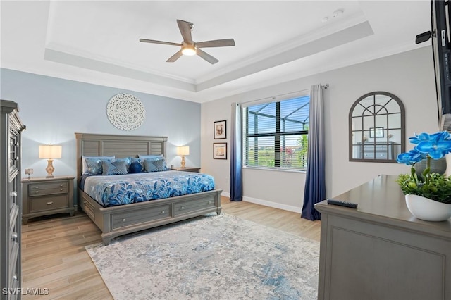 bedroom with light wood finished floors, a raised ceiling, ornamental molding, a ceiling fan, and baseboards