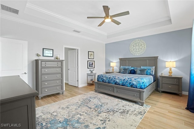 bedroom with light wood-style flooring, a raised ceiling, visible vents, and baseboards