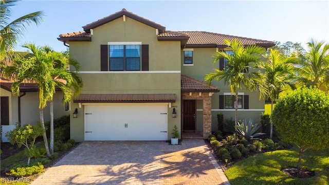 mediterranean / spanish home featuring decorative driveway, a tile roof, an attached garage, and stucco siding