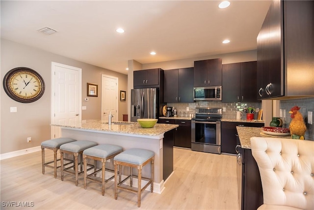 kitchen featuring light stone counters, a breakfast bar, a center island with sink, stainless steel appliances, and visible vents