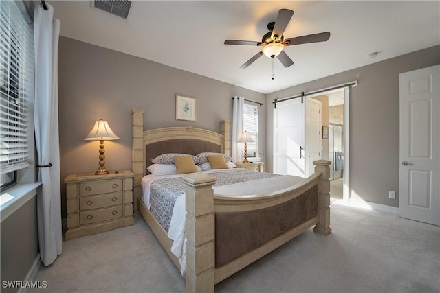 bedroom with visible vents, ensuite bathroom, a barn door, light carpet, and ceiling fan