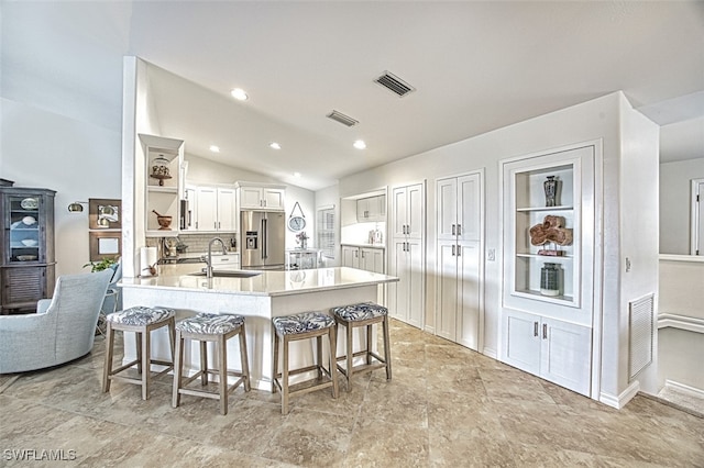 kitchen with a peninsula, a kitchen breakfast bar, light countertops, open shelves, and stainless steel fridge