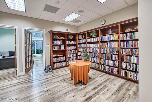 living area with wall of books, light wood finished floors, and a paneled ceiling