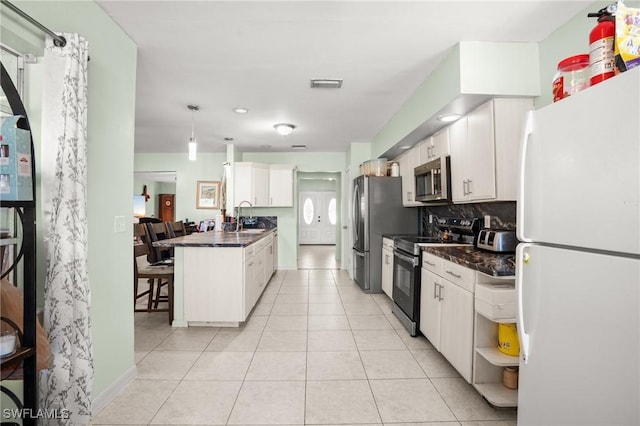 kitchen with stainless steel appliances, dark countertops, a sink, and visible vents