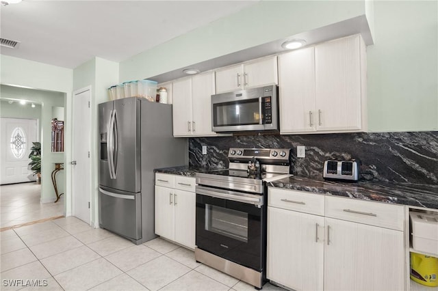 kitchen with dark stone counters, appliances with stainless steel finishes, light tile patterned flooring, and tasteful backsplash