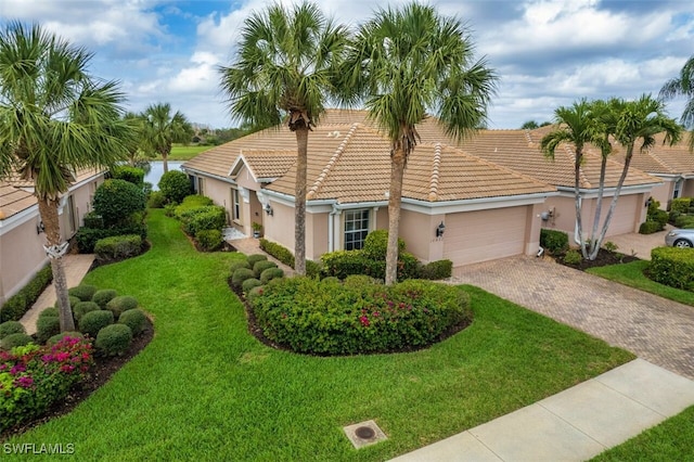 mediterranean / spanish house featuring stucco siding, a tile roof, a front yard, a garage, and decorative driveway