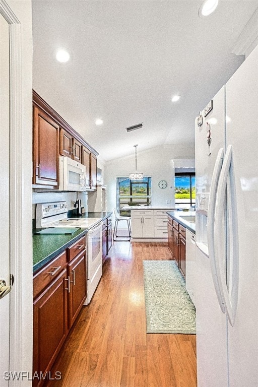 kitchen with pendant lighting, vaulted ceiling, visible vents, light wood finished floors, and white appliances