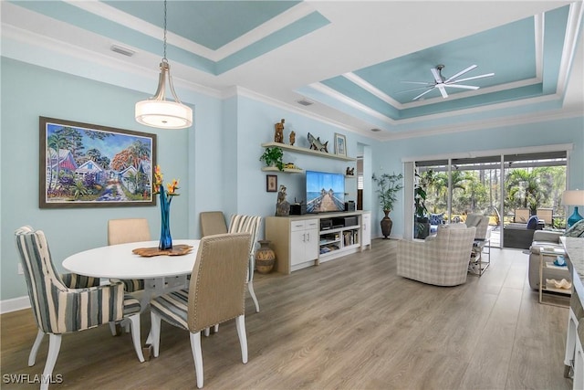 dining space with a raised ceiling, light hardwood / wood-style floors, ceiling fan, and ornamental molding