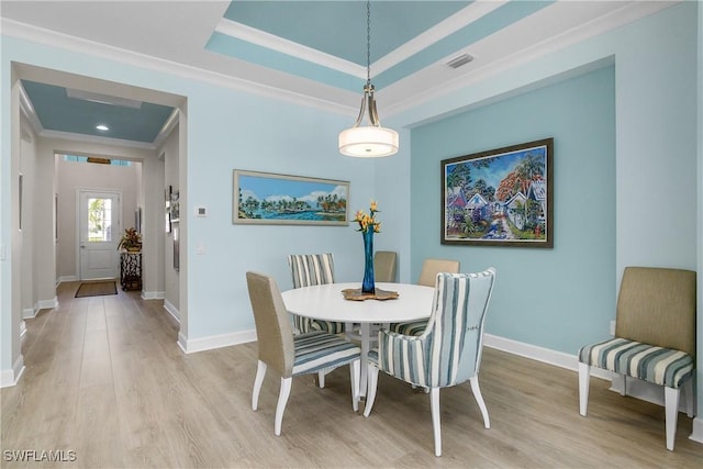 dining room featuring light hardwood / wood-style floors, a tray ceiling, and ornamental molding