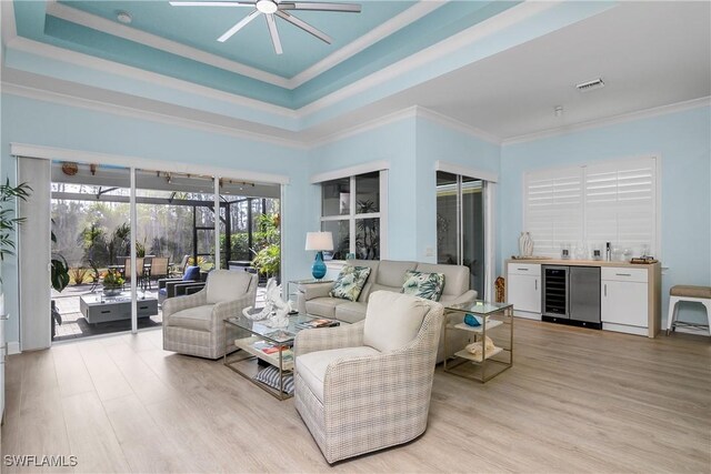 living room with ornamental molding, light hardwood / wood-style flooring, beverage cooler, and a tray ceiling