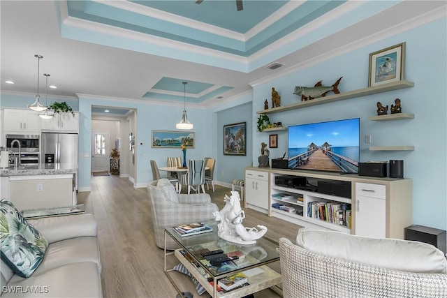 living room featuring light wood-type flooring, a tray ceiling, ornamental molding, and ceiling fan