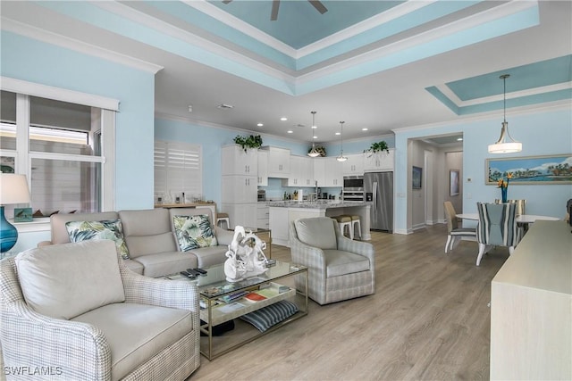 living room featuring a tray ceiling, ornamental molding, ceiling fan, and light hardwood / wood-style flooring