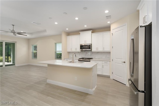 kitchen featuring white cabinetry, an island with sink, sink, a raised ceiling, and appliances with stainless steel finishes