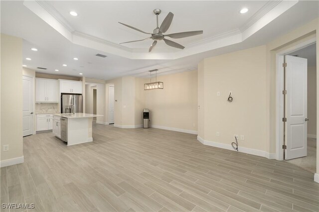 unfurnished living room featuring a tray ceiling, ornamental molding, and light wood-type flooring