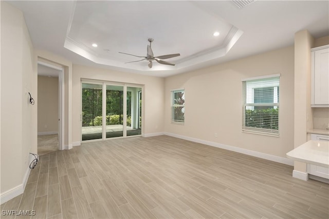 unfurnished living room with a tray ceiling, light hardwood / wood-style flooring, crown molding, and ceiling fan