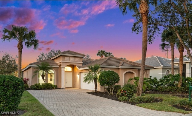 mediterranean / spanish-style house with a garage, a tiled roof, decorative driveway, and stucco siding