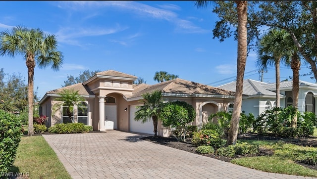 mediterranean / spanish-style house featuring an attached garage, a tile roof, decorative driveway, and stucco siding