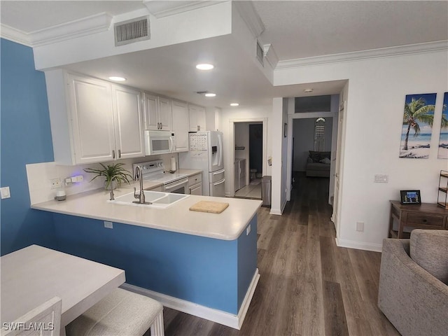 kitchen with white appliances, ornamental molding, a sink, light countertops, and dark wood finished floors