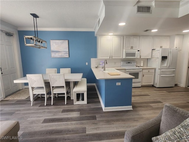 kitchen with white appliances, ornamental molding, dark wood-style floors, a peninsula, and white cabinets