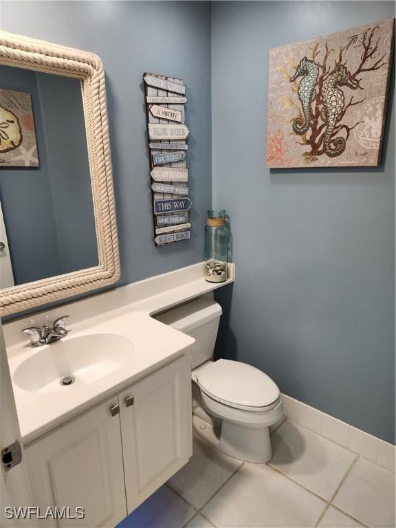half bath featuring tile patterned floors, vanity, toilet, and baseboards