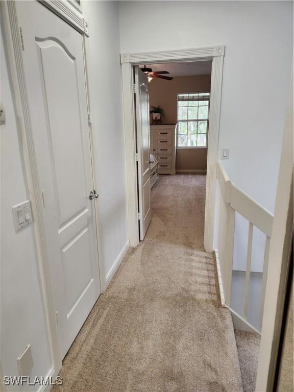 hallway with light colored carpet and an upstairs landing