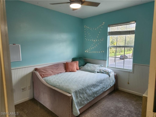 carpeted bedroom with a wainscoted wall, baseboards, and a ceiling fan