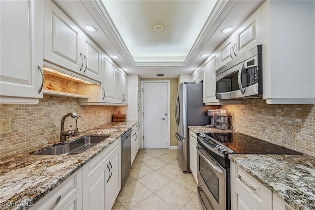 kitchen with appliances with stainless steel finishes, light stone countertops, white cabinets, a tray ceiling, and a sink