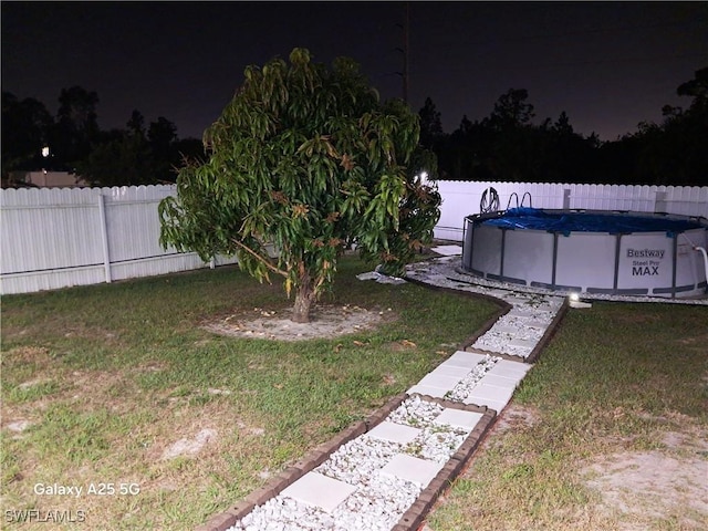 yard at night featuring an outdoor pool and a fenced backyard