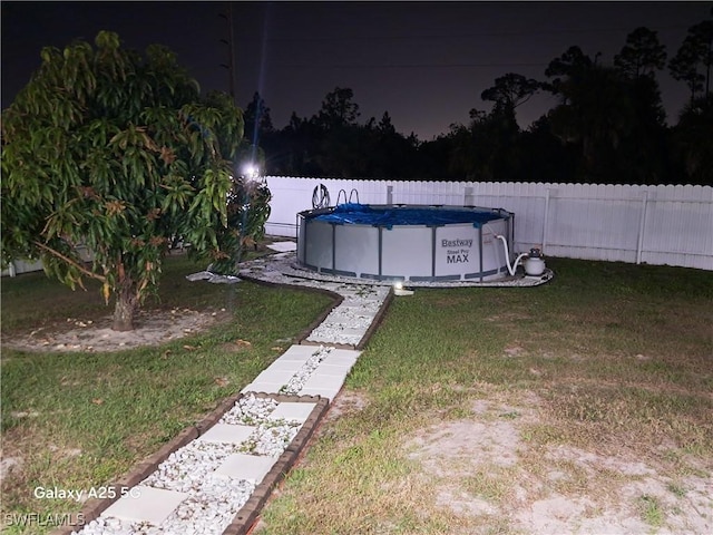 yard at night featuring a fenced in pool and a fenced backyard
